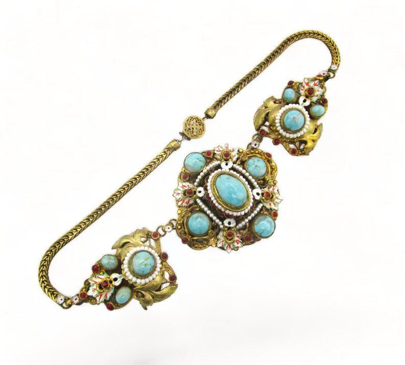Peut inclure: Un collier en or avec une cha&icirc;ne et trois pendentifs orn&eacute;s. Chaque pendentif pr&eacute;sente une pierre turquoise entour&eacute;e de pierres plus petites et d'accents rouges et blancs.