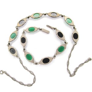 Puede incluir: Un collar de plata con una cadena delicada y piedras ovaladas de color verde, negro y gris.