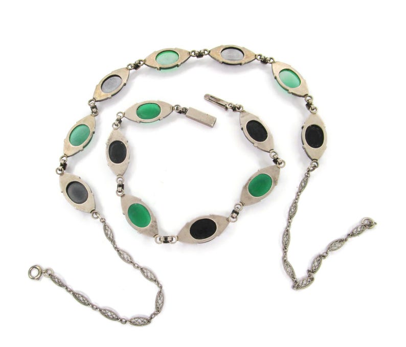 Puede incluir: Un collar de plata con una cadena delicada y piedras ovaladas de color verde, negro y gris.