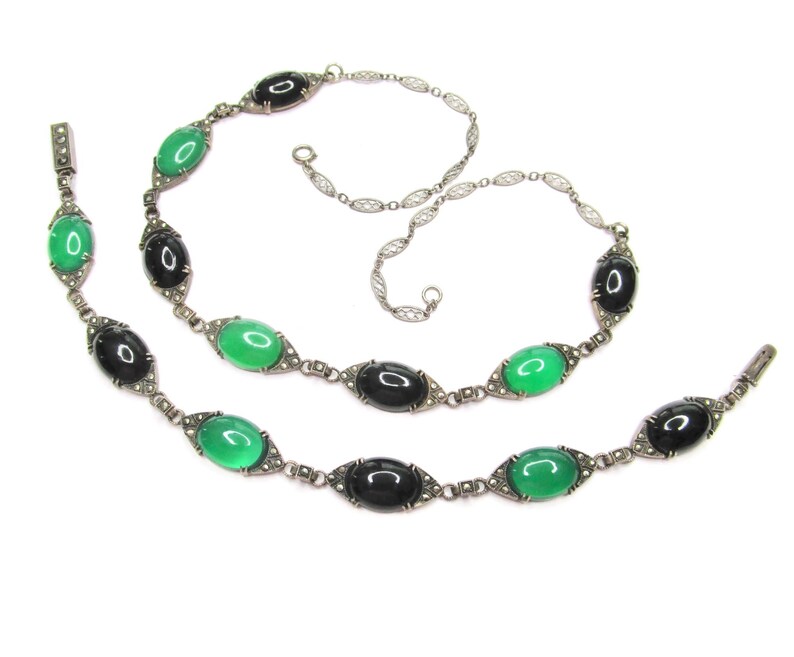 Puede incluir: Un collar y una pulsera de plata con piedras ovaladas negras y verdes. Las piedras est&aacute;n engastadas en un marco de plata con peque&ntilde;os detalles plateados.