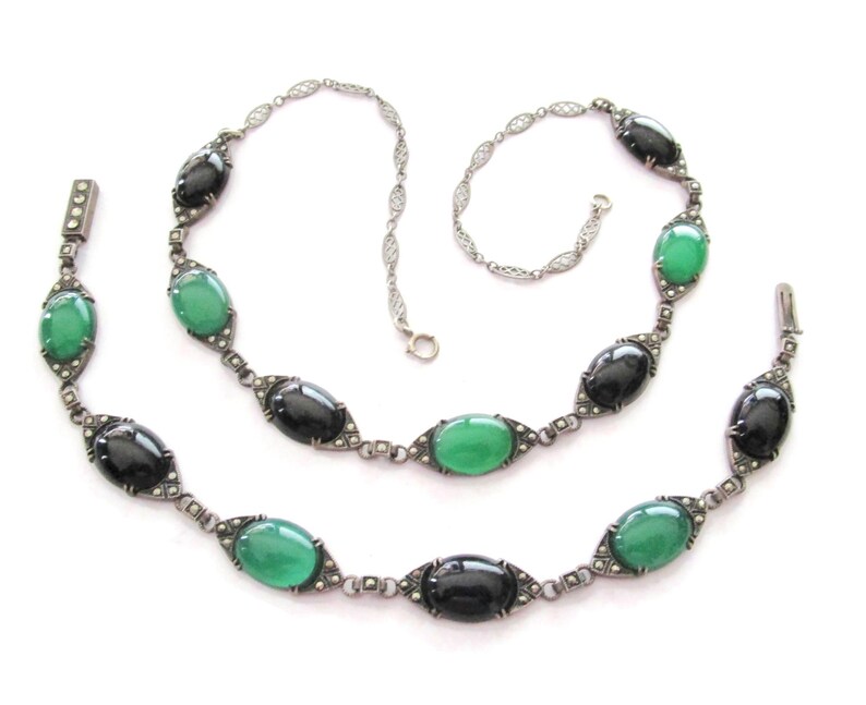 Puede incluir: Un collar vintage de plata con piedras ovaladas negras y verdes. El collar est&aacute; hecho de una cadena delicada con un dise&ntilde;o de filigrana. Las piedras est&aacute;n engastadas en plata y est&aacute;n rodeadas de peque&ntilde;as piedras brillantes.