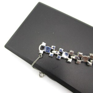 Puede incluir: Un brazalete plateado con un dise&ntilde;o de cadena y brillantes transparentes. El brazalete est&aacute; sobre una superficie negra.