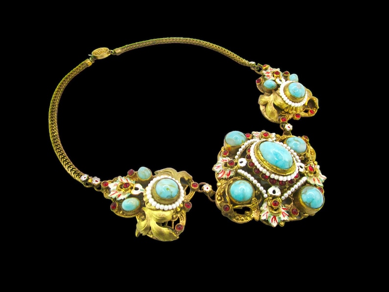 Peut inclure: Un collier en or avec des pierres turquoise et rouges. Le collier a un grand pendentif orn&eacute; avec un motif floral.
