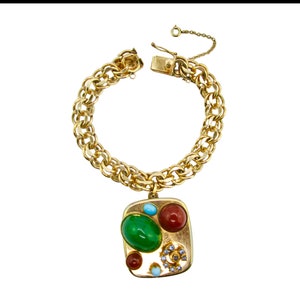 May include: A gold chain bracelet with a square charm featuring a cluster of colorful stones, including green, red, blue, and white.