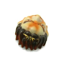 May include: A ceramic figurine of a person's face with a brown beard and moustache. The face is painted with orange, white and black details.