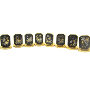 May include: Set of eight gold-rimmed black place card holders with intricate silver and gold designs depicting Japanese scenes.
