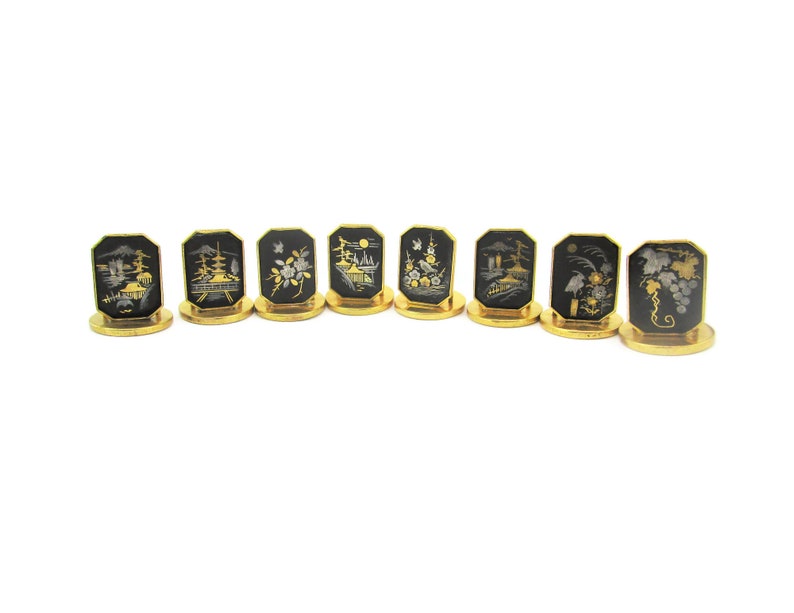 May include: Set of eight gold-rimmed black place card holders with intricate silver and gold designs depicting Japanese scenes.
