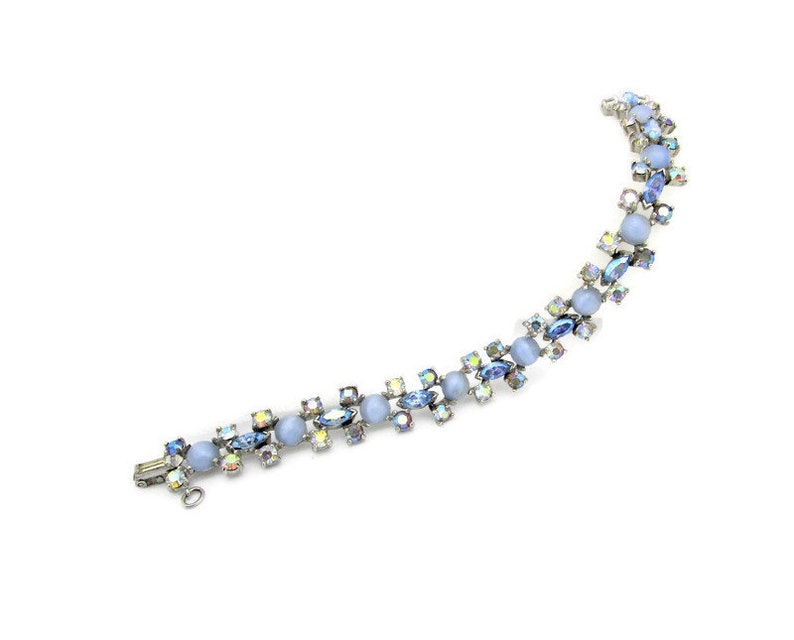 Puede incluir: Un delicado brazalete de cristal azul e iridiscente con cierre plateado. El brazalete presenta cristales redondos y en forma de marquesa alternados.