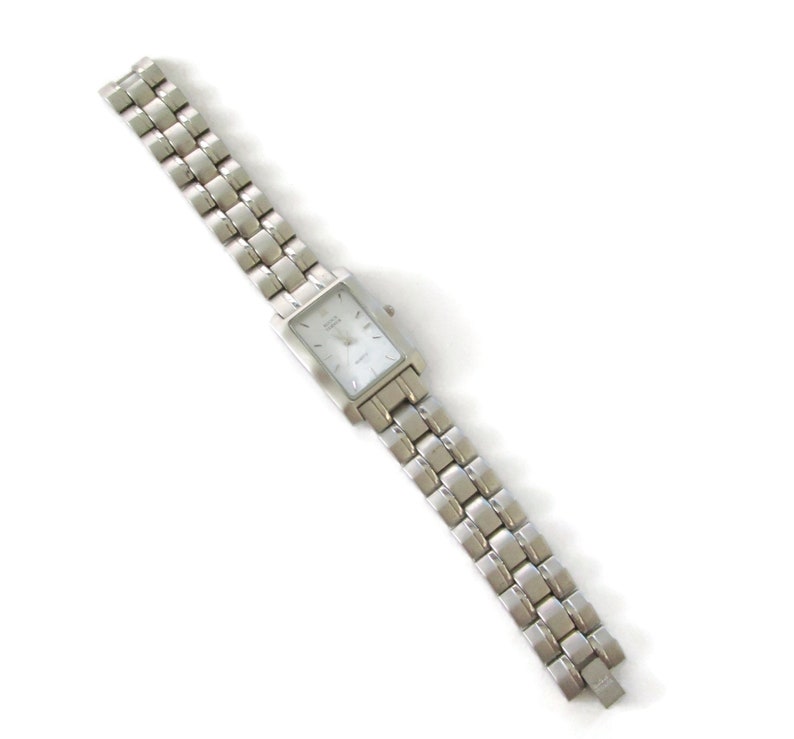 May include: A silver watch with a rectangular face and a silver metal band. The watch has a white face with black markings.