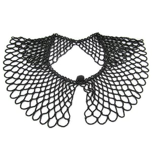 Puede incluir: Un collar de cuentas negro con un diseño delicado y calado. El collar presenta un borde festoneado y un pequeño cierre redondo en la parte delantera. El intrincado trabajo de cuentas crea un patrón similar a una red.