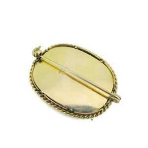 Puede incluir: Broche ovalada dorada con un borde de cuerda. La parte posterior de la broche tiene un pasador y una marca que dice "UNO 14K".