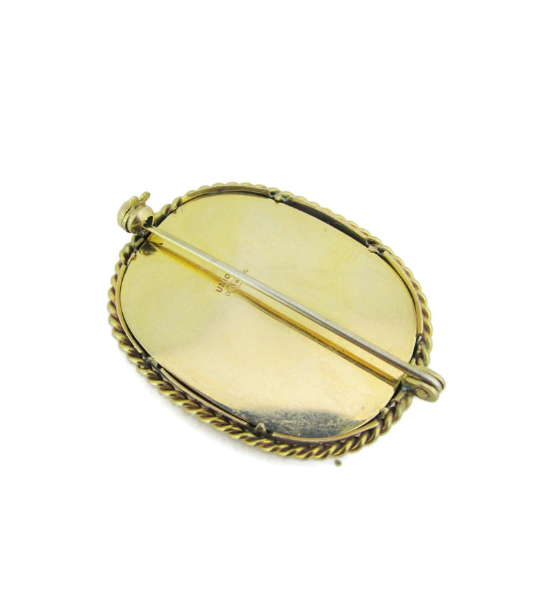 Puede incluir: Broche ovalada dorada con un borde de cuerda. La parte posterior de la broche tiene un pasador y una marca que dice "UNO 14K".