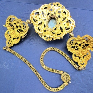 Peut inclure: Un collier en filigrane dor&eacute; avec un pendentif en pierre bleue. Le collier a une cha&icirc;ne avec deux fermoirs d&eacute;coratifs.