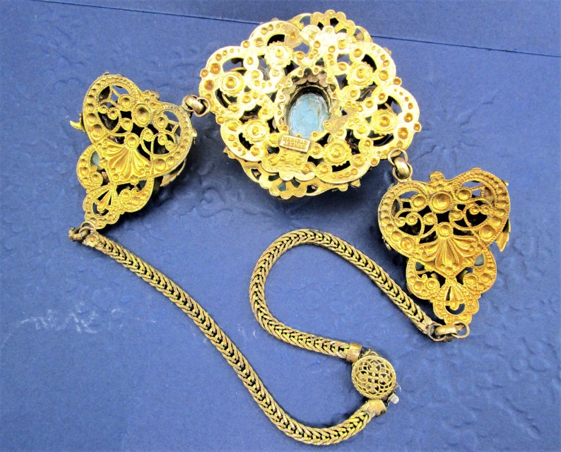 Peut inclure: Un collier en filigrane dor&eacute; avec un pendentif en pierre bleue. Le collier a une cha&icirc;ne avec deux fermoirs d&eacute;coratifs.