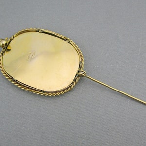 Puede incluir: Broche ovalada dorada con un borde de cuerda. La parte posterior de la broche tiene un pasador y una marca del fabricante que dice "UNION MADE".