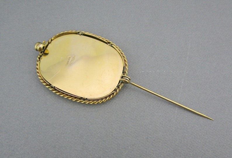 Puede incluir: Broche ovalada dorada con un borde de cuerda. La parte posterior de la broche tiene un pasador y una marca del fabricante que dice "UNION MADE".