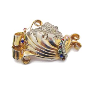 May include: A gold and silver tone brooch with a swirl design and a cluster of clear rhinestones. The brooch is accented with colorful stones in red, blue, and green.