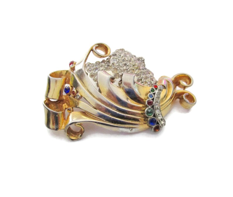May include: A gold and silver tone brooch with a swirl design and a cluster of clear rhinestones. The brooch is accented with colorful stones in red, blue, and green.