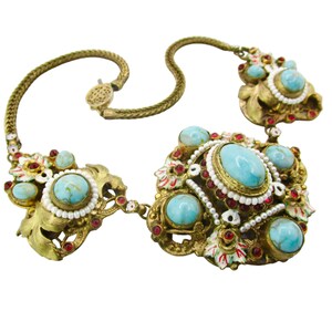 Peut inclure: Un collier en or avec un grand centre en turquoise et pierre rouge. Le collier est fait d'une cha&icirc;ne avec un fermoir et a un motif floral.