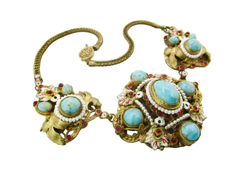 Peut inclure: Un collier en or avec un grand centre en turquoise et pierre rouge. Le collier est fait d'une cha&icirc;ne avec un fermoir et a un motif floral.