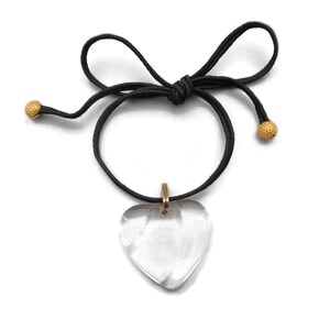 May include: A clear heart-shaped crystal pendant hangs from a black cord necklace with gold-toned beads at the ends.