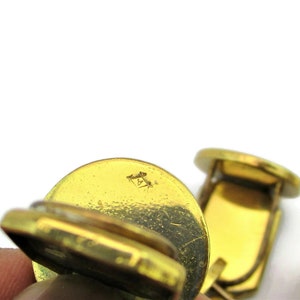 May include: A pair of gold-toned cufflinks with a textured surface. The cufflinks have a small, engraved mark on the back.