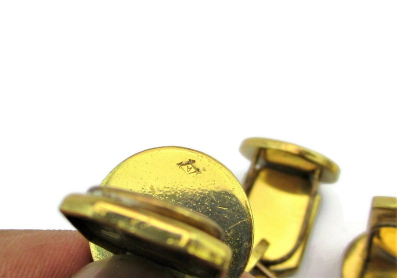 May include: A pair of gold-toned cufflinks with a textured surface. The cufflinks have a small, engraved mark on the back.