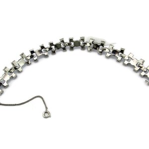 Puede incluir: Un brazalete de tono plateado con un dise&ntilde;o de cadena de eslabones. El brazalete est&aacute; hecho de metal y tiene un cierre de broche.