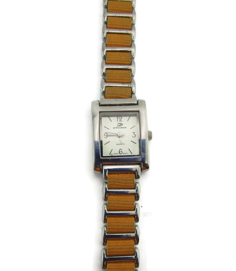 May include: A silver and orange wristwatch with a square face. The watch face is white with black markings and the word "STONE" printed on it. The watch has a quartz movement.