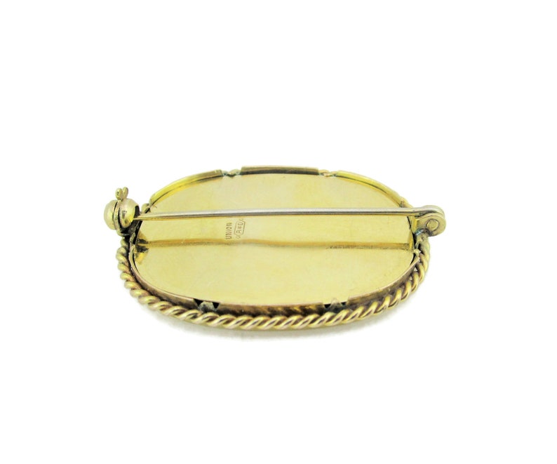 Puede incluir: Broche ovalada dorada con un borde de cuerda y un pasador en la parte posterior. La parte posterior de la broche est&aacute; marcada con "ITALY 18K GOLD".