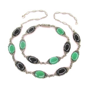 Puede incluir: Un collar largo de cadena de plata con piedras ovaladas negras y verdes alternas. Las piedras est&aacute;n engastadas en plata con un dise&ntilde;o geom&eacute;trico. La cadena est&aacute; hecha de peque&ntilde;as cuentas de plata.