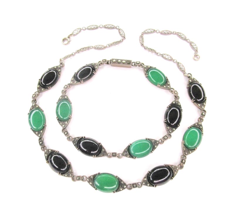 Puede incluir: Un collar largo de cadena de plata con piedras ovaladas negras y verdes alternas. Las piedras est&aacute;n engastadas en plata con un dise&ntilde;o geom&eacute;trico. La cadena est&aacute; hecha de peque&ntilde;as cuentas de plata.