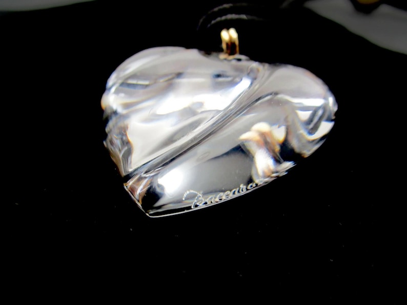 May include: A clear crystal heart pendant necklace with a gold chain and the word "Baccarat" engraved on the heart.