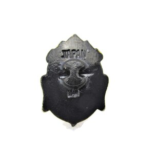 May include: Black metal pin with a detailed design. The back of the pin has the word "JAPAN" printed on it.