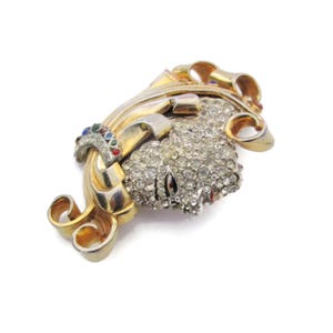 May include: A gold tone brooch with a swirl design and a cluster of clear rhinestones. The brooch has a few small colored stones in the design.