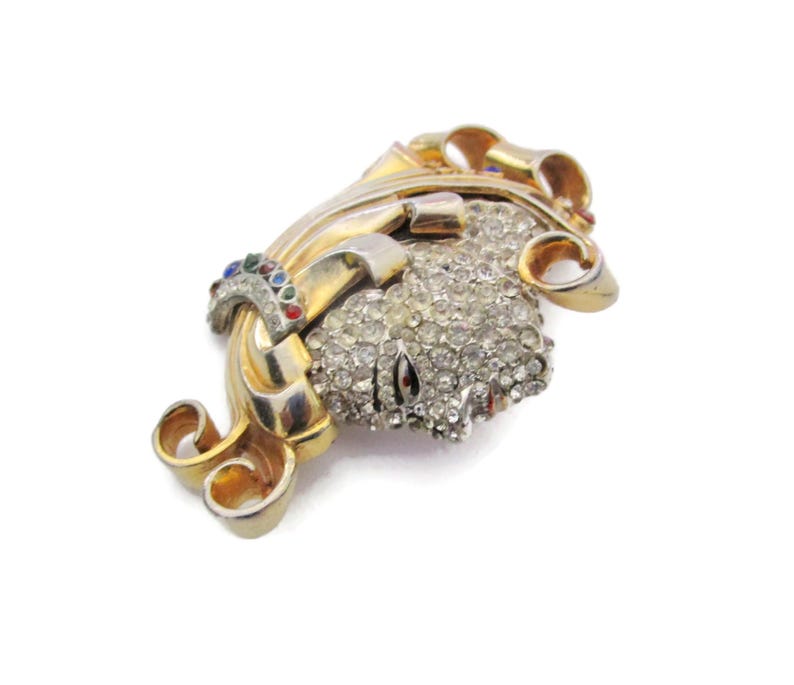 May include: A gold tone brooch with a swirl design and a cluster of clear rhinestones. The brooch has a few small colored stones in the design.