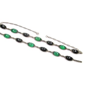 Puede incluir: Un collar de plata con piedras ovaladas negras y verdes alternas. El collar est&aacute; hecho de una cadena delicada con peque&ntilde;as cuentas de plata.