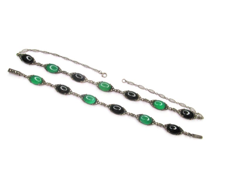 Puede incluir: Un collar de plata con piedras ovaladas negras y verdes alternas. El collar est&aacute; hecho de una cadena delicada con peque&ntilde;as cuentas de plata.