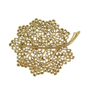 May include: A gold-toned leaf-shaped brooch with a delicate, intricate design. The brooch is made of metal and has a filigree pattern.