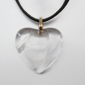 May include: A clear heart-shaped pendant necklace with a gold-tone chain and a black leather cord.