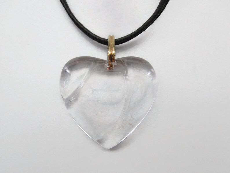May include: A clear heart-shaped pendant necklace with a gold-tone chain and a black leather cord.
