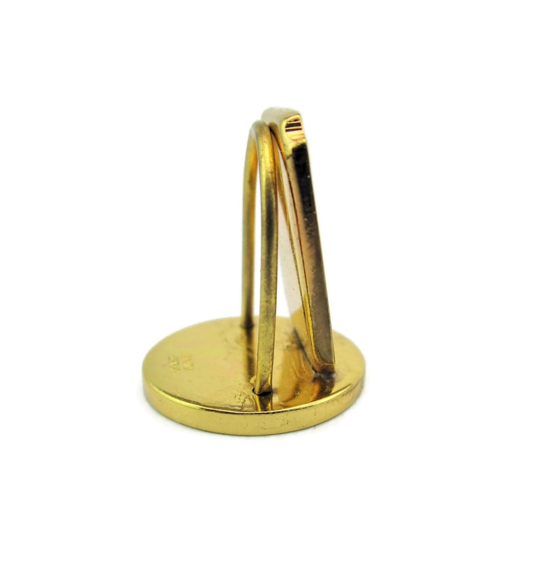 May include: Gold-toned metal picture frame stand with a round base and a rectangular frame. The stand is designed to hold a small picture or photo.