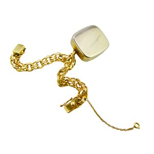 May include: A gold chain bracelet with a square-shaped pendant. The pendant is made of a silver-toned metal and has a smooth, polished finish.