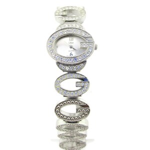 May include: Silver-tone watch with a white face and a band made of interlocking 'G's encrusted with clear rhinestones. The watch face has a small '12' and 'Coleen' printed on it.