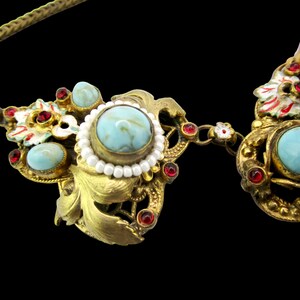 Peut inclure: Un collier en or avec des pierres turquoise et rouges, et des accents de perles blanches. Le collier a un motif floral.