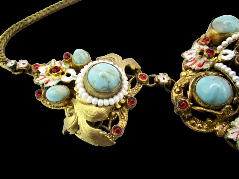 Peut inclure: Un collier en or avec des pierres turquoise et rouges, et des accents de perles blanches. Le collier a un motif floral.