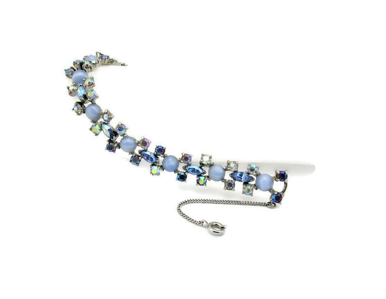 Puede incluir: Un delicado brazalete de cristal azul e iridiscente con un extensor de cadena. El brazalete presenta un patr&oacute;n repetitivo de piedras azules y cristales transparentes.