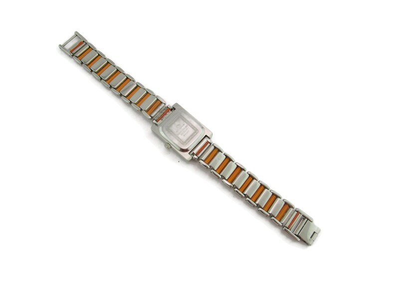 May include: A silver and orange watch with a square face and a metal band.