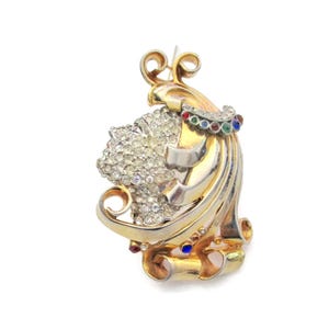 May include: A gold and silver tone brooch with a swirling design. The brooch is decorated with clear rhinestones and colorful stones.