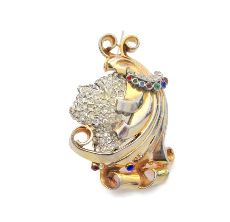 May include: A gold and silver tone brooch with a swirling design. The brooch is decorated with clear rhinestones and colorful stones.